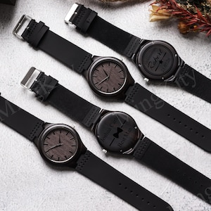 K&ouml;nnte beinhalten: Vier Holzuhren mit schwarzen Lederarmb&auml;ndern werden gezeigt. Die Zifferbl&auml;tter der Uhren haben eine dunkle Holzmaserung, und die R&uuml;ckseiten von zwei Uhren haben eingravierten Text. Einer sagt "Groomman Robert 21.07.26" und der andere "Joshua Carter Best Man".