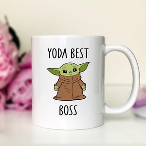 Pu&ograve; includere: Tazza in ceramica bianca con un'illustrazione a cartoni animati di un personaggio alieno verde con una veste marrone. Il testo "YODA BEST BOSS" &egrave; stampato in nero sopra e sotto il personaggio.