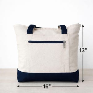 Pu&ograve; includere: Borsa tote in tela color crema con dettagli blu navy. Ha una tasca con cerniera e manici blu navy. La borsa misura 40.6 cm di larghezza e 33 cm di altezza.