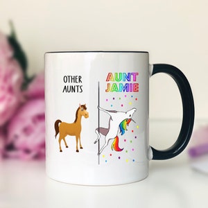 May include: White ceramic mug with a black rim and handle. The mug has a graphic of a unicorn doing a pole dance with the text "Aunt Jamie" and a horse with the text "Other Aunts".