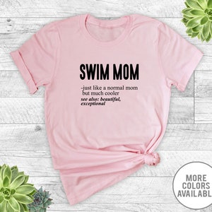 May include: Pink t-shirt with the text "SWIM MOM - just like a normal mom but much cooler see also: beautiful, exceptional" printed on it.