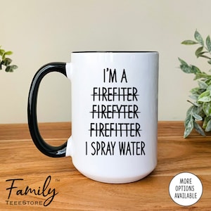 Op de afbeelding: Een witte keramische mok met een zwarte rand en handvat. De mok heeft zwarte tekst met de tekst "I'm a Firefighter Firefyter Firefitter I Spray Water".