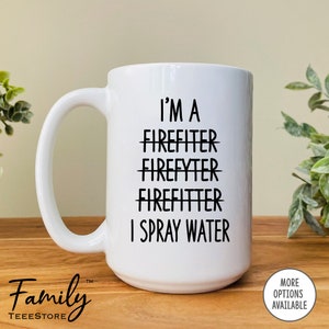 Op de afbeelding: Een witte keramische mok met een zwart ontwerp dat zegt "Ik ben een brandweerman, ik spuit water". Het woord "Brandweerman" is drie keer doorgehaald.