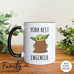 May include: White ceramic mug with a black rim and handle. The mug features a cartoon image of a green baby Yoda character with the text "YODA BEST ENGINEER".