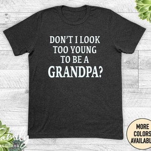 May include: Dark grey t-shirt with white text that reads "Don't I look too young to be a Grandpa?"