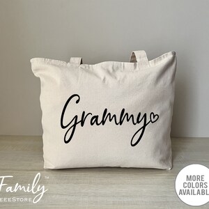K&ouml;nnte beinhalten: Eine wei&szlig;e Canvas-Tragetasche mit schwarzen Henkeln und dem Wort "Grammy" in Kursivschrift mit einem Herzsymbol.