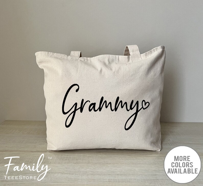 K&ouml;nnte beinhalten: Eine wei&szlig;e Canvas-Tragetasche mit schwarzen Henkeln und dem Wort "Grammy" in Kursivschrift mit einem Herzsymbol.