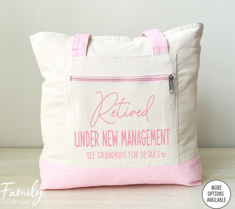 May include: A white canvas tote bag with pink handles and a pink zippered pocket. The bag has the text "Retired Under New Management See Grandkids for Details" printed on it in pink.