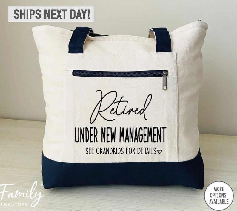 May include: A white canvas tote bag with black handles and a black zippered pocket. The bag has black text that reads "Retired Under New Management See Grandkids for Details".