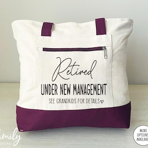 May include: A white canvas tote bag with a purple bottom. The bag has a zippered pocket and the text "Retired Under New Management See Grandkids for Details" printed on the front.