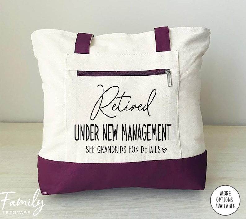 May include: A white canvas tote bag with a purple bottom. The bag has a zippered pocket and the text "Retired Under New Management See Grandkids for Details" printed on the front.