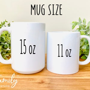 Puede incluir: Dos tazas de cer&aacute;mica blanca, una de 15 oz y otra de 11 oz, sobre una superficie de madera. Las tazas son ambas blancas con texto negro.