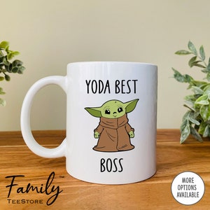 Pu&ograve; includere: Tazza in ceramica bianca con un manico grande, con la scritta "YODA BEST BOSS" e un'illustrazione di un personaggio alieno verde con una veste marrone. La tazza ha il logo Family TeeStore.