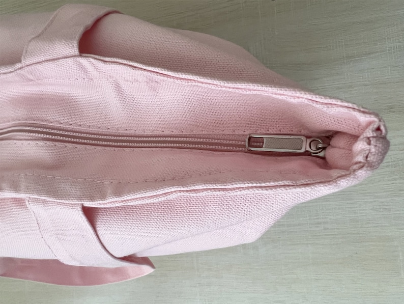 K&ouml;nnte beinhalten: Eine rosa Canvas-Tragetasche mit Rei&szlig;verschluss. Der Rei&szlig;verschluss ist silberfarben und hat einen Schieber.