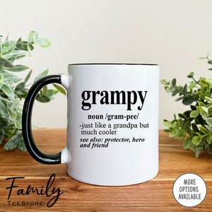 May include: White ceramic coffee mug with a black handle and rim. The mug has black text that reads "grampy" and a definition of the word. The text reads "noun/gram-pee/-just like a grandpa but much cooler see also: protector, hero and friend"