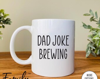 Op de afbeelding: Witte keramische koffiemok met zwarte tekst die "Dad Joke Brewing" luidt.
