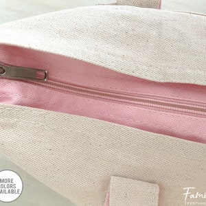 Puede incluir: Primer plano de una cremallera en una bolsa de lona rosa y blanca. La cremallera es plateada y tiene un tirador. La bolsa est&aacute; hecha de un material de lona suave y duradero.