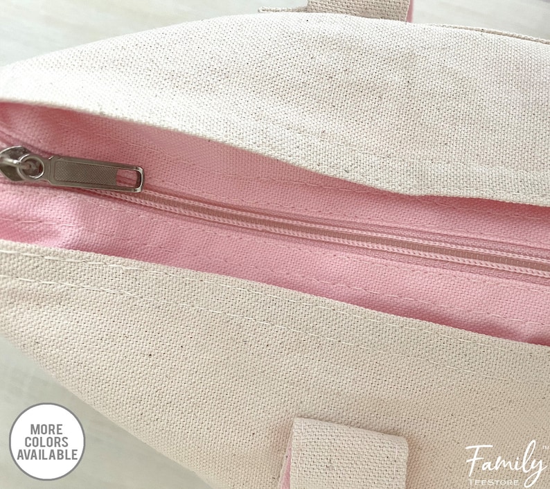 Puede incluir: Primer plano de una cremallera en una bolsa de lona rosa y blanca. La cremallera es plateada y tiene un tirador. La bolsa est&aacute; hecha de un material de lona suave y duradero.