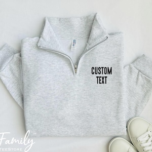 May include: A gray half-zip sweatshirt with the text "CUSTOM TEXT" printed on the front.
