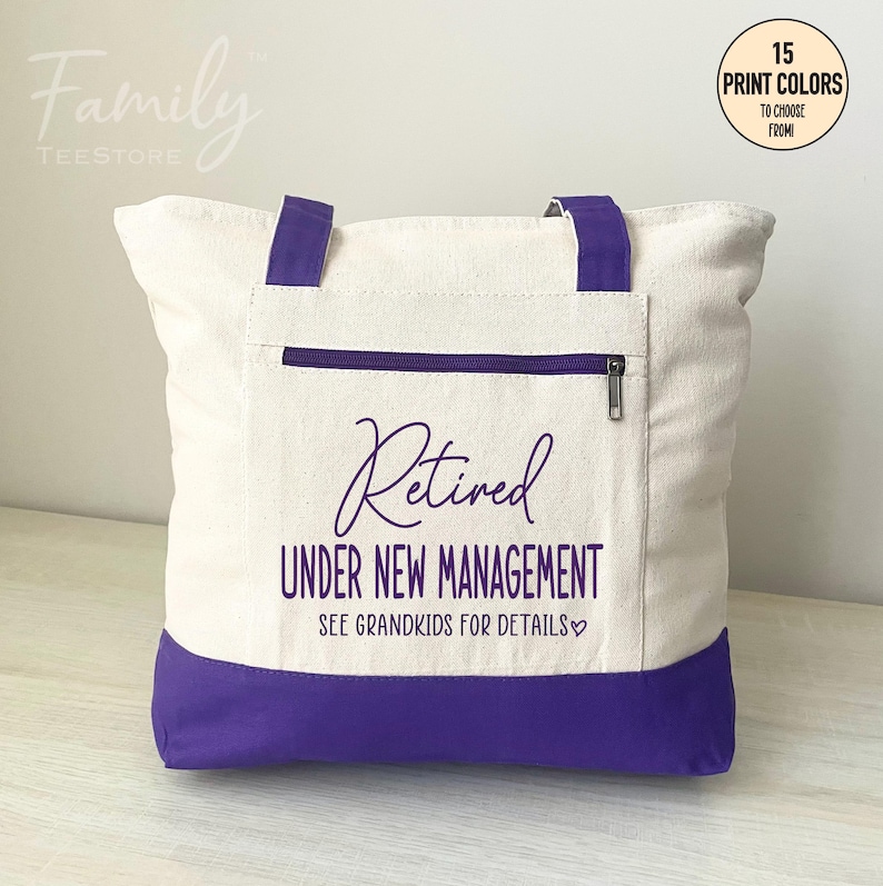 May include: A white canvas tote bag with purple handles and a purple bottom. The bag has a zippered pocket on the front and the text "Retired Under New Management See Grandkids for Details" printed in purple.