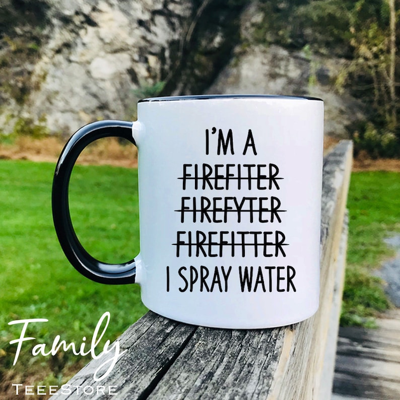 Op de afbeelding: Een witte keramische mok met een zwarte rand en handvat. De mok heeft zwarte tekst die "I'm a Firefighter Firefyter Firefitter I Spray Water" zegt.