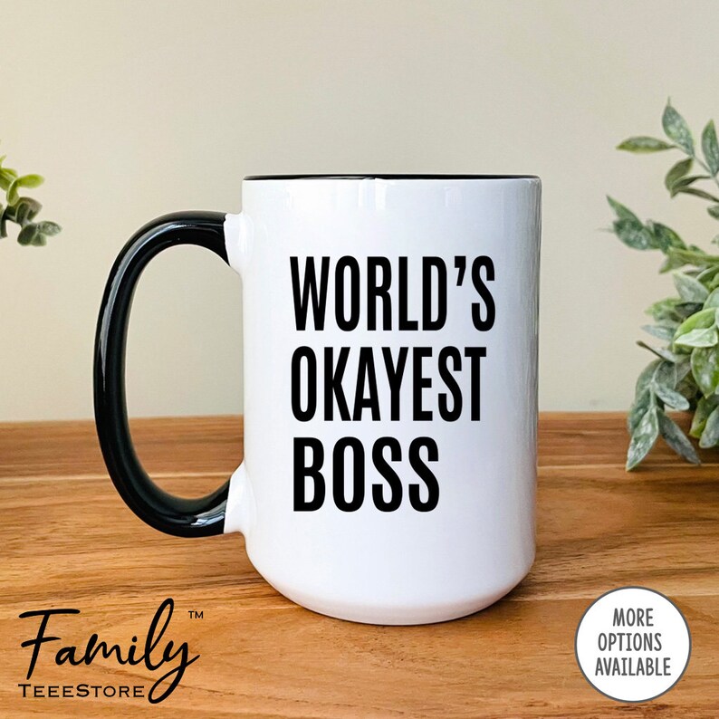 May include: White ceramic mug with a black rim and handle. The mug has black text that reads "WORLD'S OKAYEST BOSS".