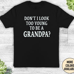 May include: Black t-shirt with white text that reads "Don't I look too young to be a grandpa?"
