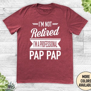 May include: Red t-shirt with white text that reads "I'm not retired I'm a professional Pap Pap".