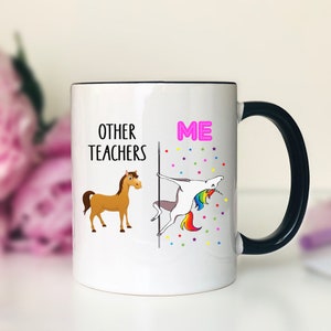 May include: White ceramic mug with a black handle. The mug has a graphic of a horse on the left side and a unicorn on the right side. The text "Other Teachers" is above the horse and the text "ME" is above the unicorn.