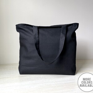 K&ouml;nnte beinhalten: Eine schwarze Canvas-Tragetasche mit zwei Henkeln. Die Tasche ist aus dickem, strapazierf&auml;higem Canvas gefertigt und hat ein schlichtes, klassisches Design.