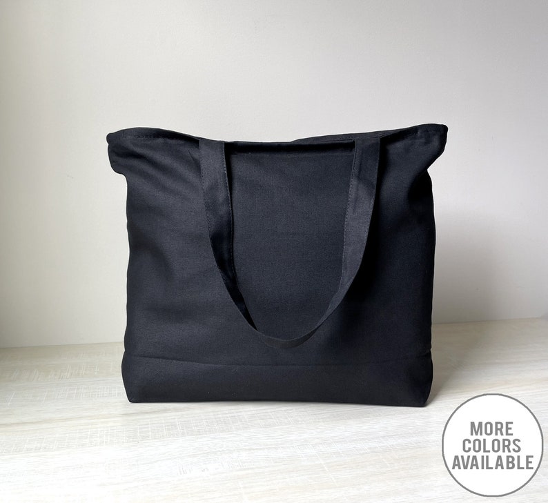 K&ouml;nnte beinhalten: Eine schwarze Canvas-Tragetasche mit zwei Henkeln. Die Tasche ist aus dickem, strapazierf&auml;higem Canvas gefertigt und hat ein schlichtes, klassisches Design.
