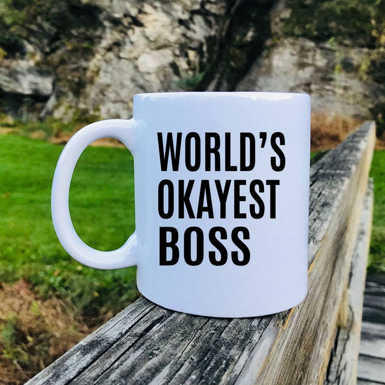 May include: White ceramic coffee mug with black text that reads "WORLD'S OKAYEST BOSS".