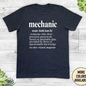 May include: A dark heather grey t-shirt with white text that reads "mechanic" and a definition of the word. The definition is "noun/muh-kan-ik/ -someone who does precision guesswork based on unreliable data provided by those of questionable knowledge see also: wizard, magician"