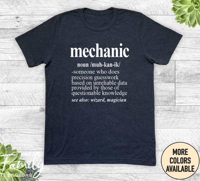 May include: A dark heather grey t-shirt with white text that reads "mechanic" and a definition of the word. The definition is "noun/muh-kan-ik/ -someone who does precision guesswork based on unreliable data provided by those of questionable knowledge see also: wizard, magician"