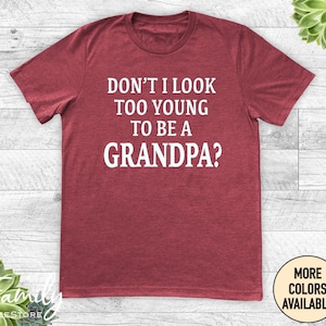 May include: Red t-shirt with white text that reads "Don't I look too young to be a grandpa?"