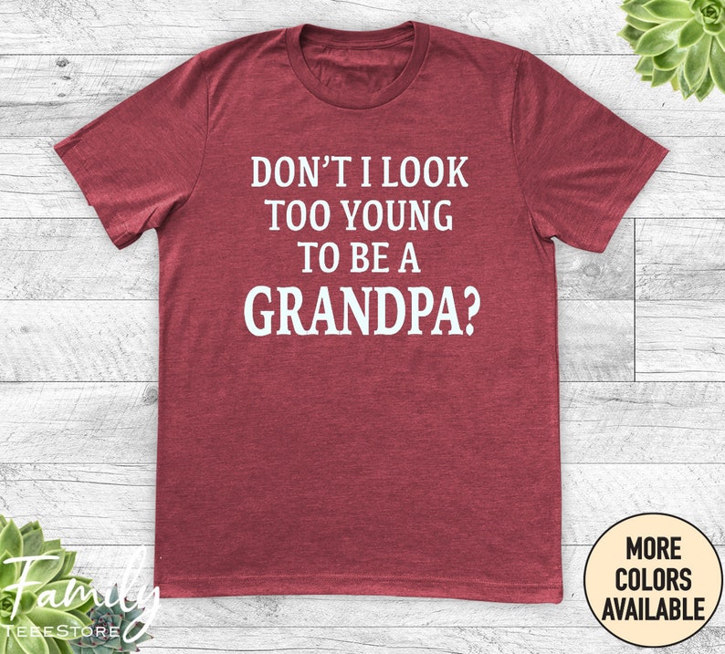 May include: Red t-shirt with white text that reads "Don't I look too young to be a grandpa?"