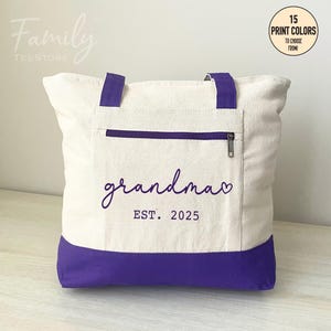Puede incluir: Una bolsa de lona blanca con asas y fondo morados. La bolsa tiene un bolsillo con cremallera y dice "grandma EST. 2025" en texto morado.