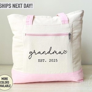 Puede incluir: Una bolsa de lona blanca con ribete rosa y un bolsillo con cremallera. La bolsa tiene el texto "grandma" con un coraz&oacute;n y "EST. 2025" impreso en ella.