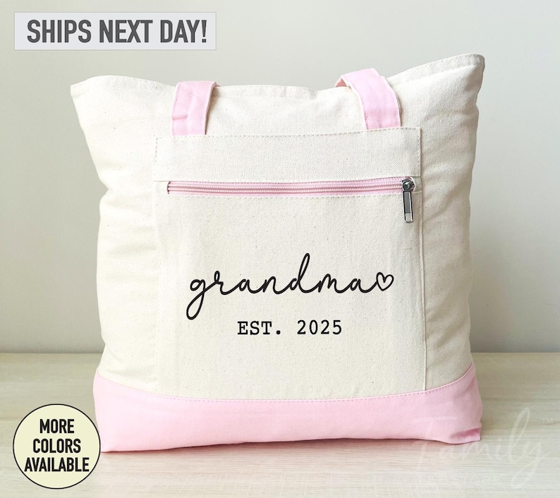 Puede incluir: Una bolsa de lona blanca con ribete rosa y un bolsillo con cremallera. La bolsa tiene el texto "grandma" con un coraz&oacute;n y "EST. 2025" impreso en ella.