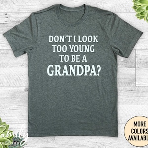 May include: A dark heather grey t-shirt with white text that reads "Don't I look too young to be a grandpa?"