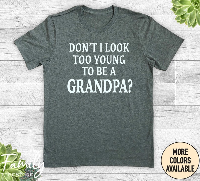 May include: A dark heather grey t-shirt with white text that reads "Don't I look too young to be a grandpa?"