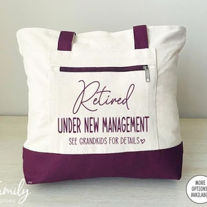 May include: A white canvas tote bag with maroon handles and a maroon bottom. The bag has a zippered pocket on the front and the text "Retired Under New Management See Grandkids for Details" printed in black.