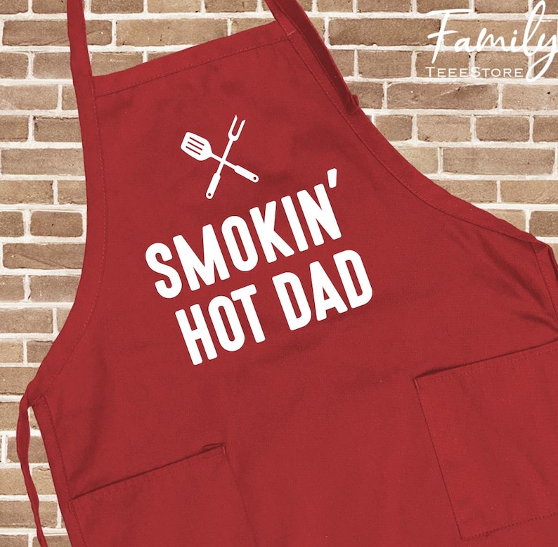 May include: A red apron featuring the text "SMOKIN' HOT DAD" in white, along with a crossed spatula and fork graphic. It has two front pockets and neck and waist ties. The apron is made of a durable fabric.