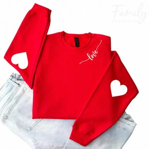 May include: Red sweatshirt with white hearts on the sleeves and the word "love" written in cursive on the front.