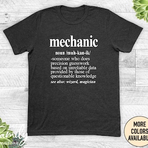 May include: A dark grey t-shirt with a white graphic that defines the word "mechanic" as someone who does precision guesswork based on unreliable data provided by those of questionable knowledge. The graphic also says "see also: wizard, magician".