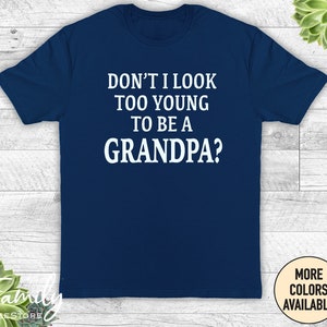 May include: Navy blue t-shirt with white text that reads "Don't I look too young to be a grandpa?"