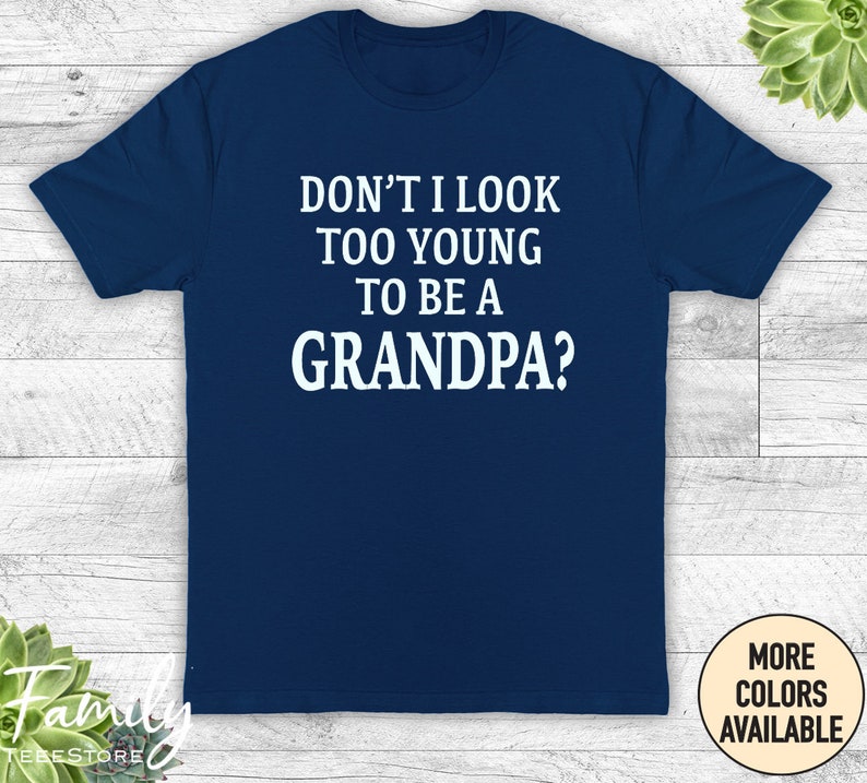 May include: Navy blue t-shirt with white text that reads "Don't I look too young to be a grandpa?"