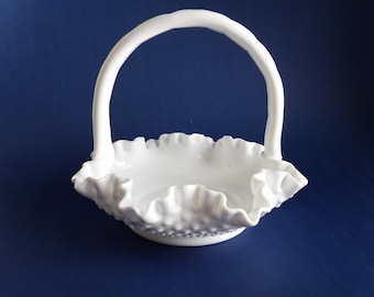 May include: White milk glass basket with a ruffled edge and a handle. The basket is made of a textured glass and has a delicate, feminine design.