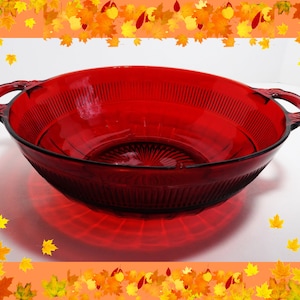 May include: A large, red glass serving bowl with two handles. The bowl has a textured, ribbed design and a slightly flared rim.