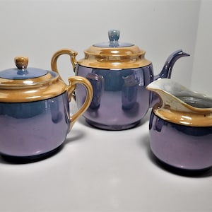 May include: A purple and gold tea set with a teapot, creamer, and sugar bowl.